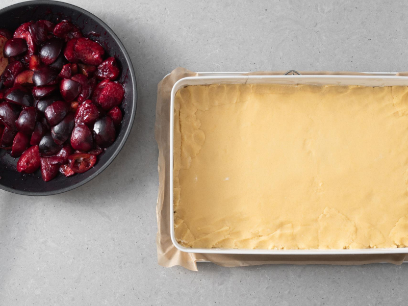 Na patelni przygotowanie śliwki, a obok forma wyłożona ciastem.