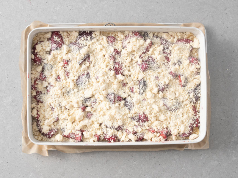 Gotowe ciasto kruche ze śliwkami i kruszonką przed pieczeniem.