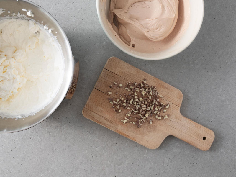 W misie ubita śmietanka. Obok pokrojone kinderki.  W drugiej misie masa z rozpuszczoną czekoladą i kinderkami.