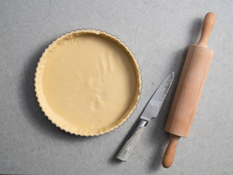 nieupieczona tarta w foremce obok nóż i wałek do ciasta