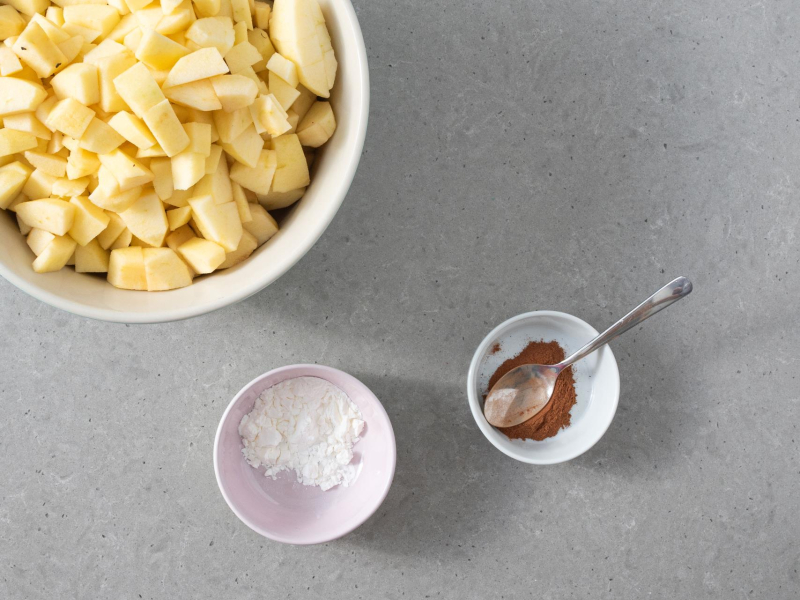 Pokrojone jabłka w misce. Obok miseczki z cynamonem oraz mąką ziemniaczaną.