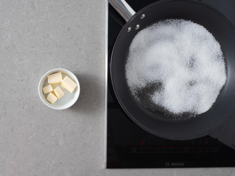 Rozsypany cukier  na patelni. Obok w miseczce masło.