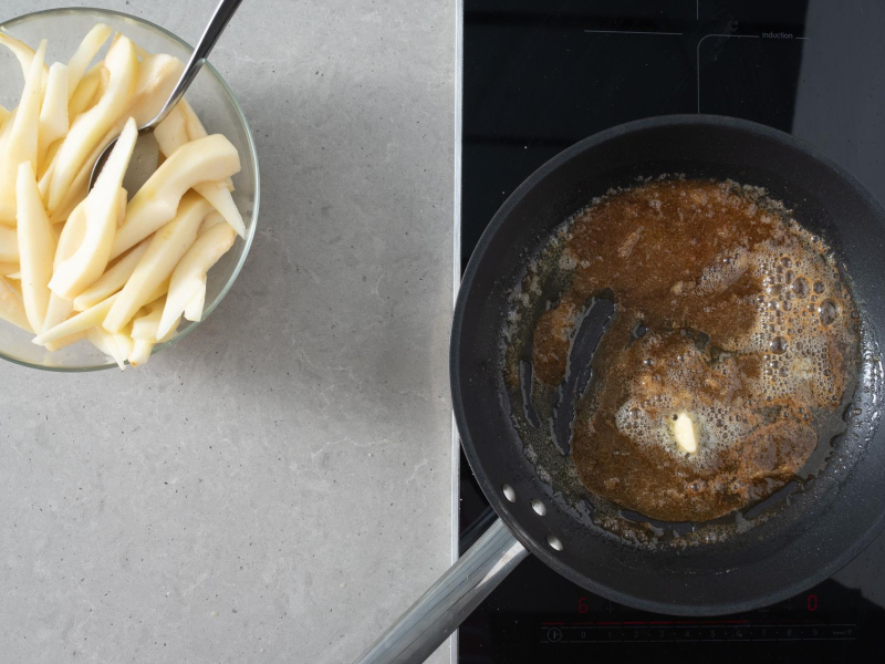 Na patelni karmel. Obok pokrojone gruszki w misce.