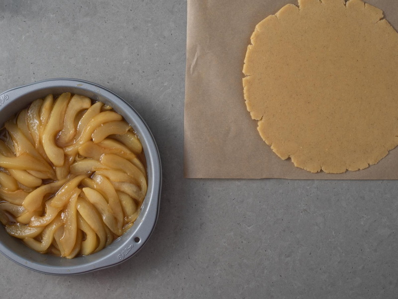 Na papierze rozwałkowane ciasto kruche. Obok gruszki w karmelu wyłożone w formie.