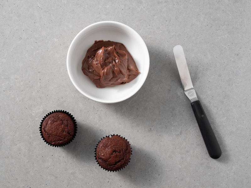 Upieczone babeczki na blacie kuchennym. Obok krem czekoladowy.