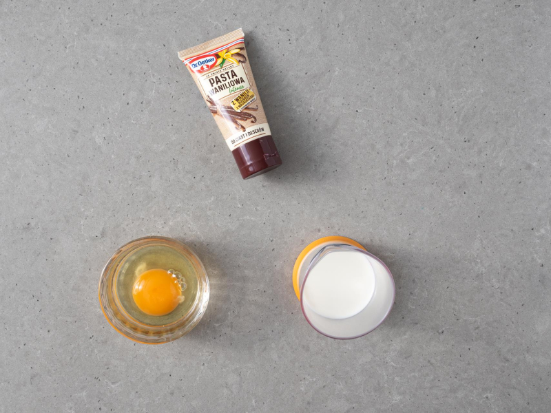 Na blacie pasta waniliowa Dr. Oetkera. Obok jajko w miseczce. W szklance mleko.