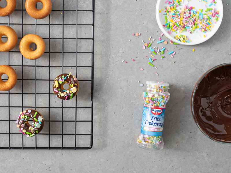 Dekorowanie mi ni donutów rozpuszczoną czekoladą i posypką cukrową.