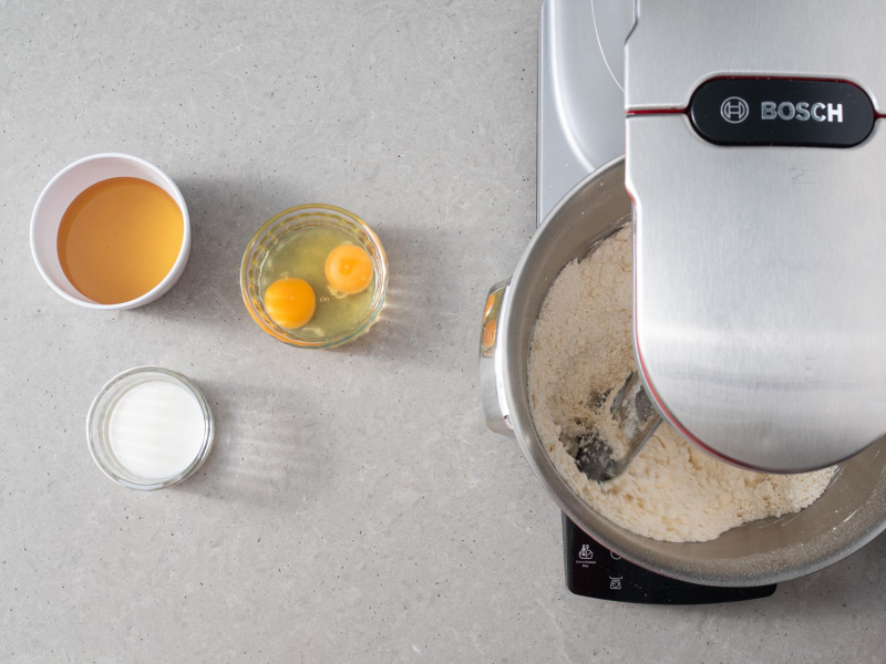 W misie rozmieszane składniki na ciasto. Obok w miseczce jajka, miód oraz mleko/