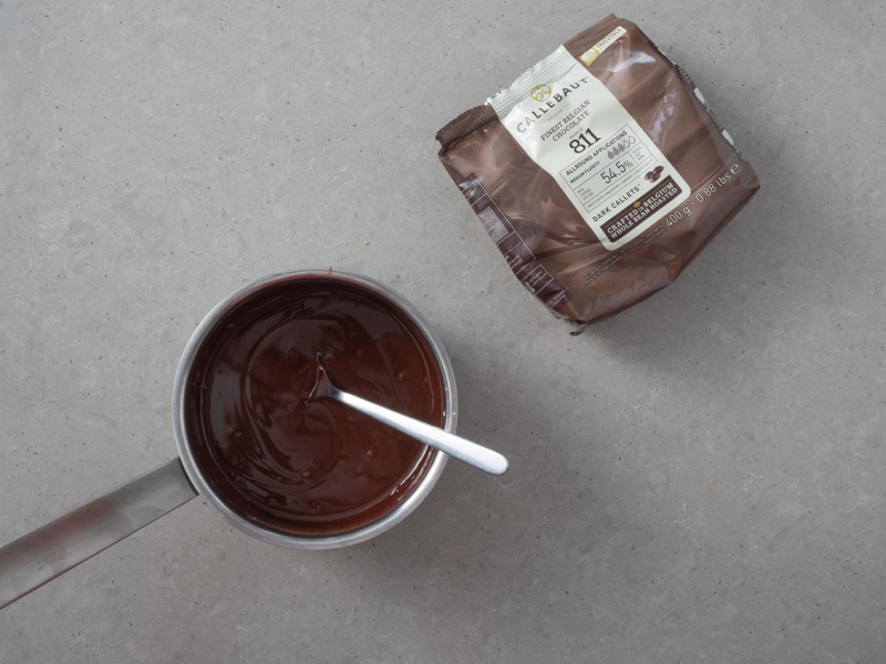 W garnku przygotowana polewa  czekoladowa. Obok czekolada firmy callebaut.
