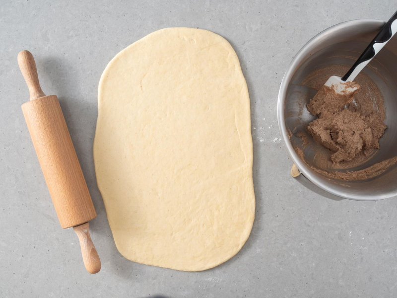 Rozwałkowane na placek ciasto drożdżowe. Obok masa cynamonowa.