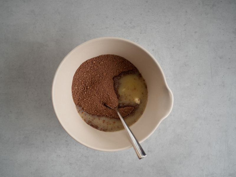 w misce na szarym blacie pokruszone herbatniki z kakao z roztopionym masłem