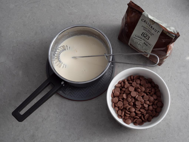 w rondelku zagotowana śmietanka obok w miseczce czekolada Callebaut