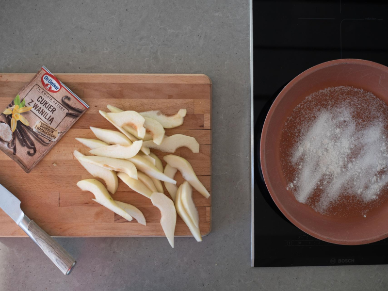 Na drewnianej desce pokrojne gruszki. Na patelni cukier.