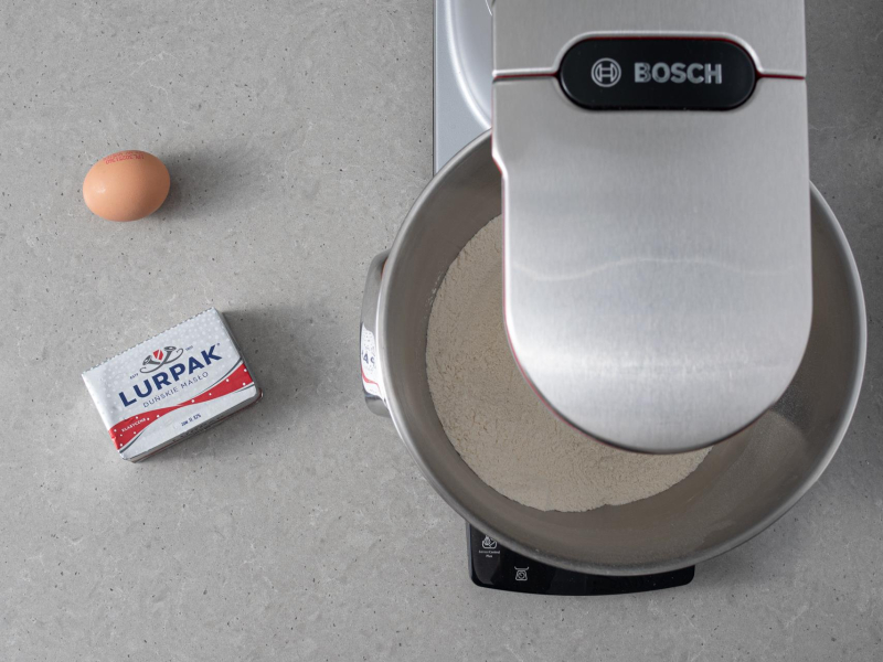 Na blacie masło lurpak, jajko oraz mąki wymieszane z cukrem w misie robota kuchennego Bosch.