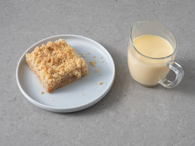 Kawałek szarlotki na talerzyku. Obok sos waniliowy w dzbanuszku.