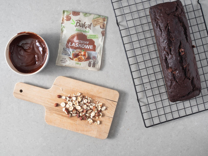 Na desce posiekane orzechy laskowe, a w miseczce polewa czekoladowa.