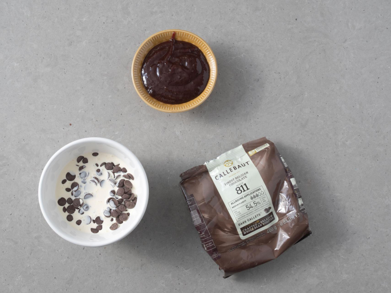 Na blacie kuchennym opakowanie czekolady Callebaut oraz w miseczkach: powidła śliwkowe i śmietanka z czekoladą.