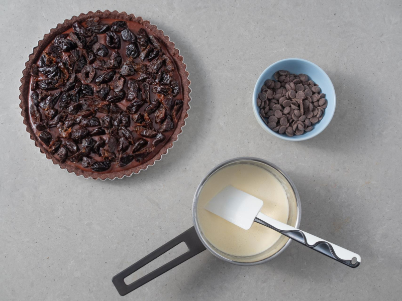 Tarta z suszonymi śliwkami. A obok w garnku śmietanka i czekolada.