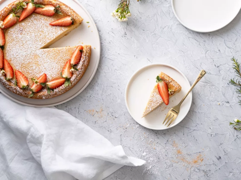 wegański sernik a'la wiedeński oprószony cukrem pudrem i udekorowany truskawkami