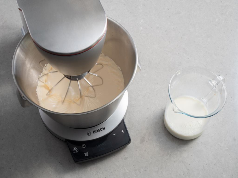 w misie robota kuchennego bosch utarte żółtka z cukrem obok mleko w szklanym naczyniu