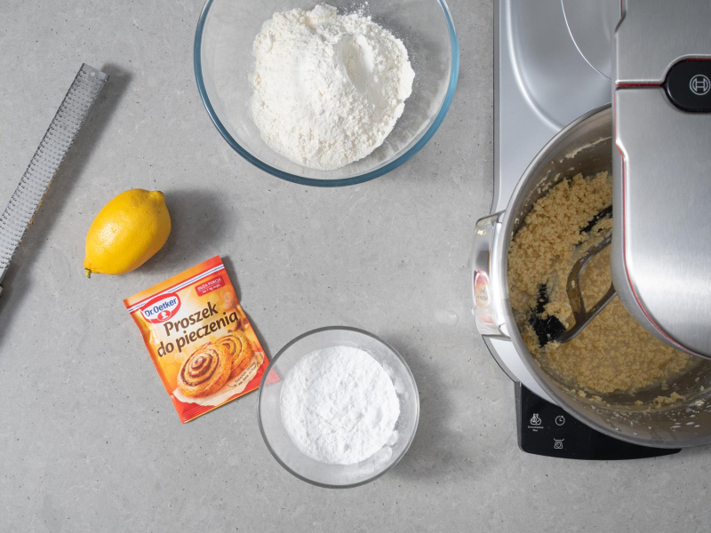 Na blacie cytryny, proszek do pieczenia Dr. Oetkera oraz mąka pszenna i skrobia ziemniaczana w miseczkach.