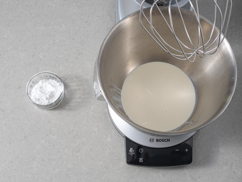 W misie miksera 艣mietanka. Obok cukier puder w miseczce.