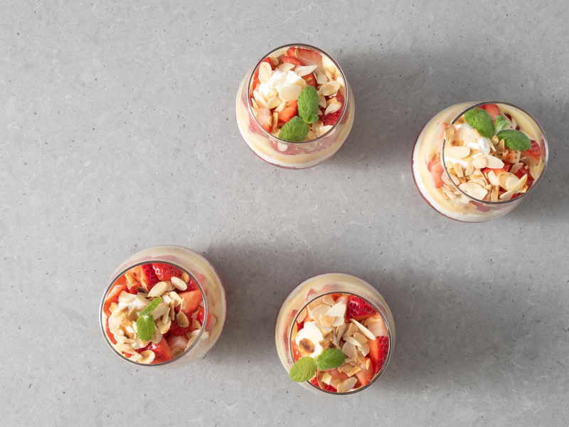 Gotowy deser trifle z truskawkami, podany z p艂atkami migda艂贸w i listkami mi臋ty.