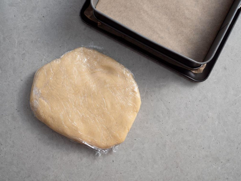 ciasto kruche owinięte folią spożywczą, obok forma do pieczenia