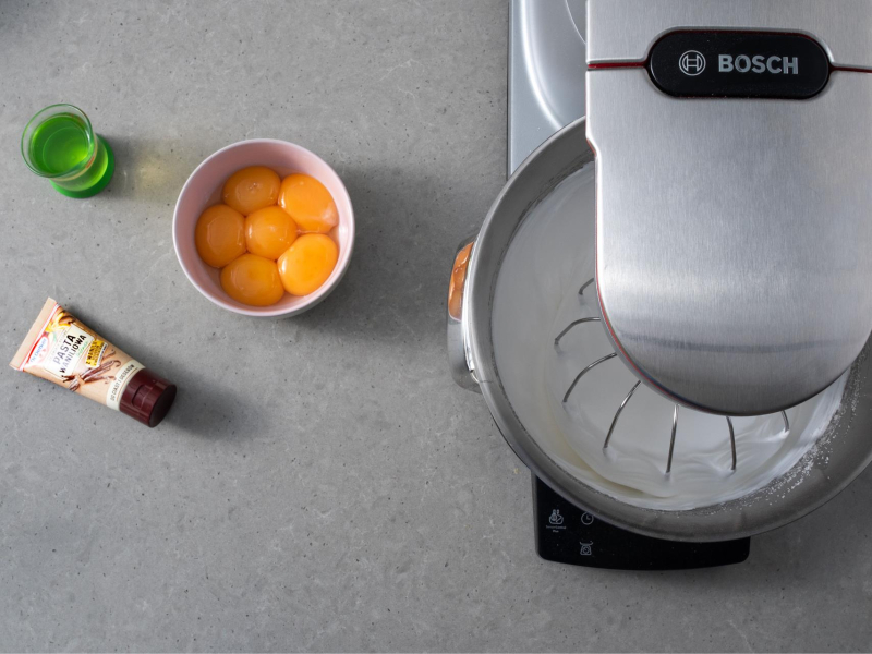 Robot kuchenny na blacie. A obok w miseczce żółtka, olej oraz pasta waniliowa.