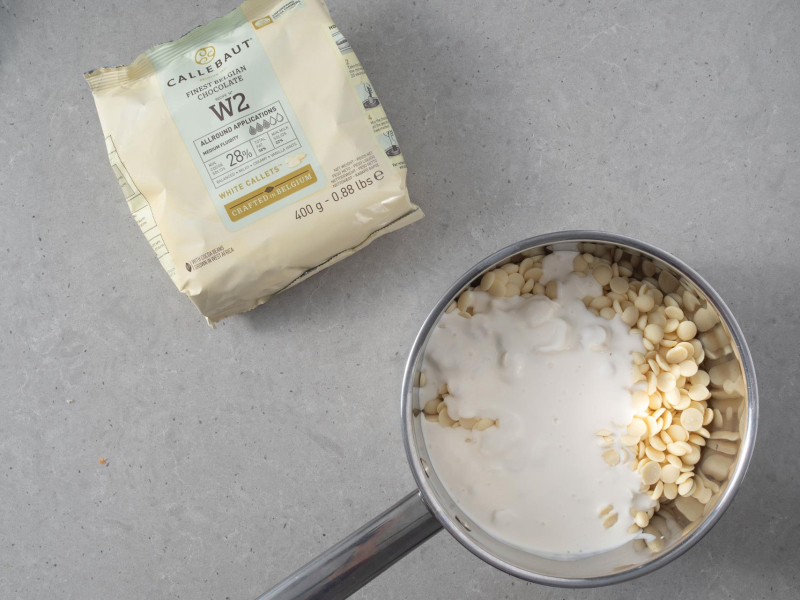 W garnku biała czekolada ze śmietanką, a obok opakowanie białej czekolady.