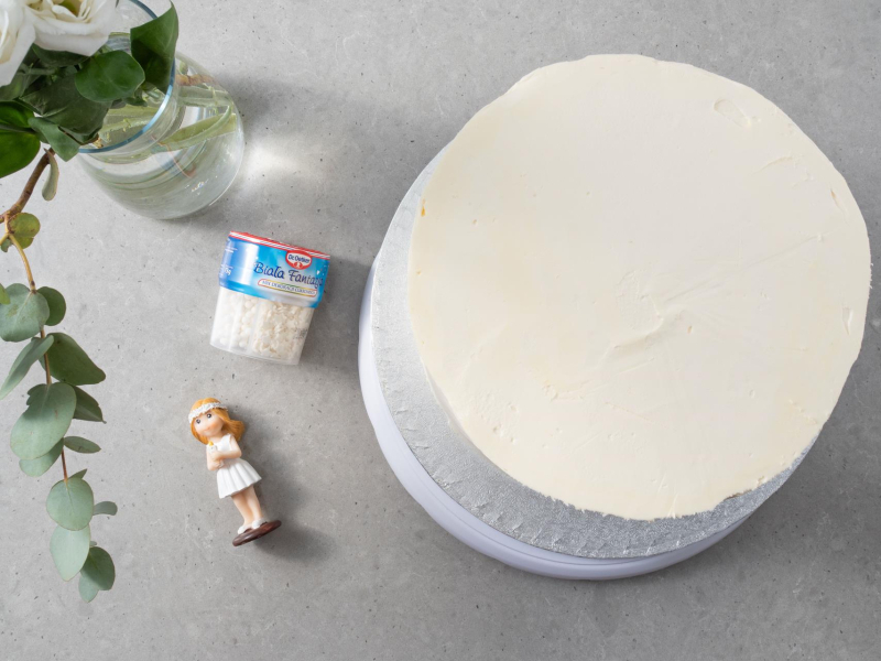 Otynkowany tort na komunię. Obok kwiaty, figurka na tort oraz mix dekoracji cukrowych.