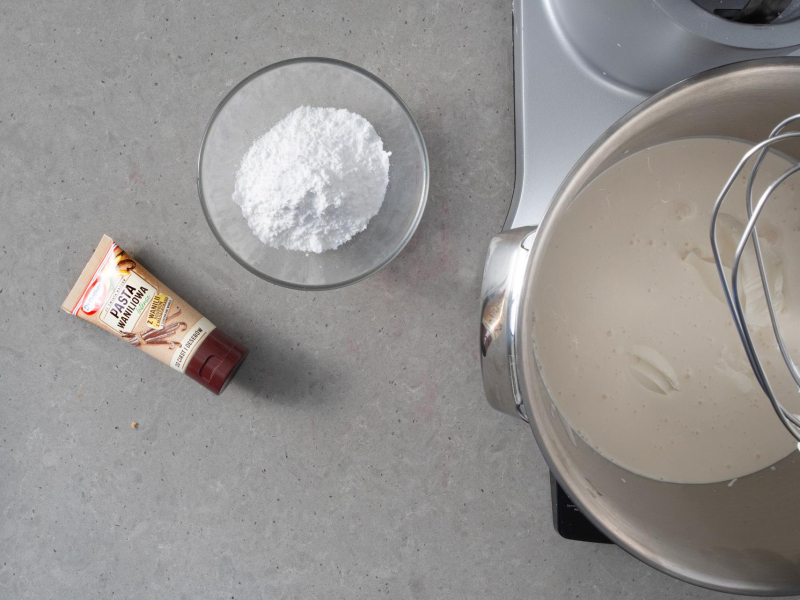 W misie miksera śmietanka oraz mascarpone. Obok cukier puder oraz opakowanie pasty waniliiowej.