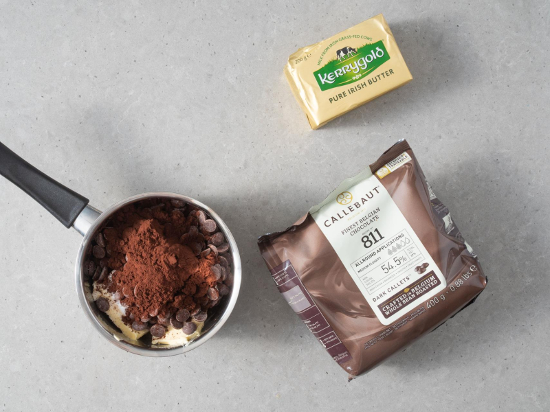 W garnku masło, czekolada oraz kakao. Obok opakowanie czekolady oraz kostka masła.