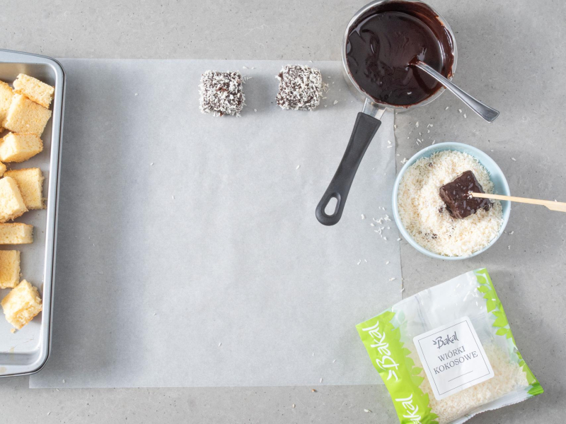 Obtaczanie kawałków ciasta kokosowego w polewie czekoladowej i wiórkach kokosowych.