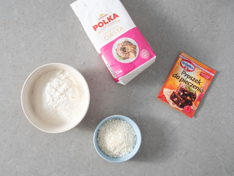 W misie mąka pszenna, obok wiórki kokosowe. Na blacie opakowanie mąki pszennej oraz proszku do pieczenia.