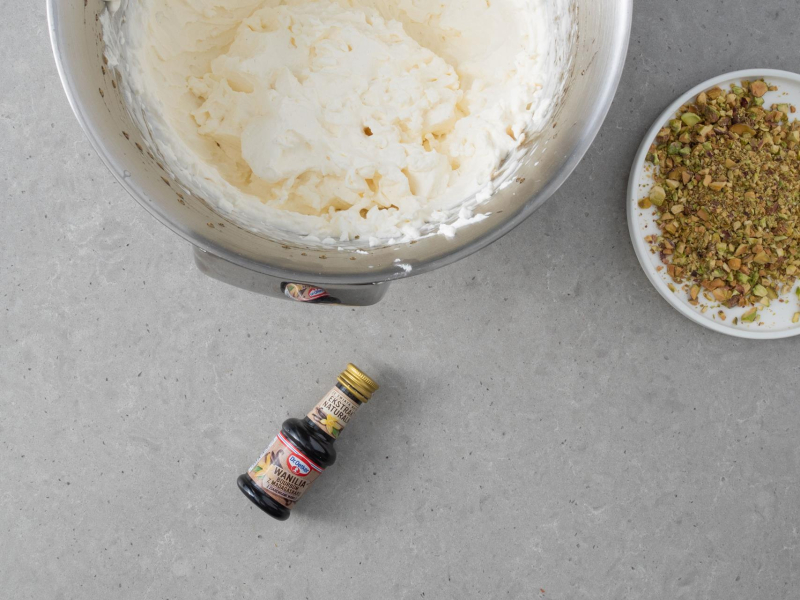 W misie miksera gotowy krem śmietankowy. Obok posiekane pistacje i ekstrakt waniliowy.
