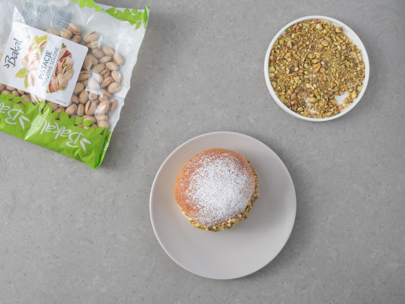 Gotowa bułeczka maritozzi na talerzyku. Obok posiekane pistacje.