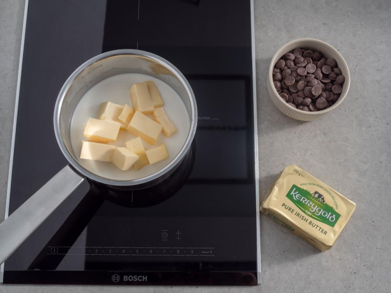 na kuchence indukcyjnej bosch w rondelku mleko z masłem lurpak, obok w miseczce kaletki czekolady