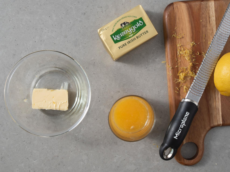 na desce otarta skórka z cytryny obok maśło lurpak i sok z pomarańczy