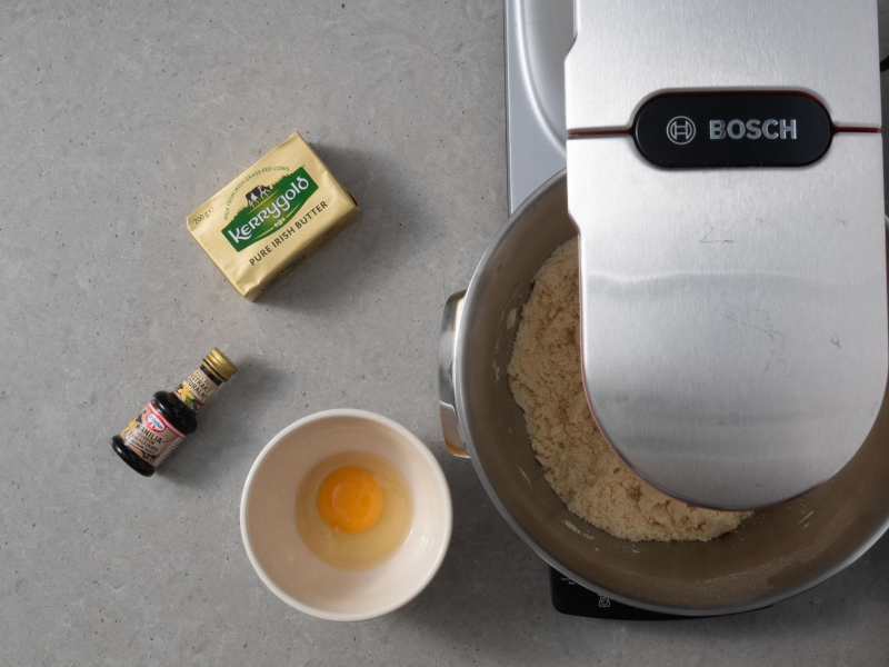 Na blacie robot kuchenny firmy Bosch. Obok w miseczkach składniki do ciasta kruchego i kostka masła kerrygold.