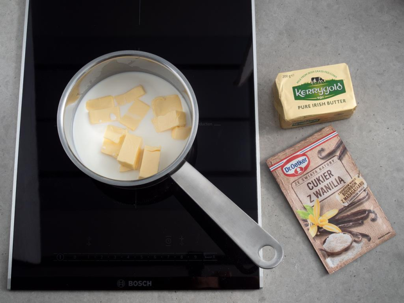 Na blacie masło, cukier z wanilią oraz garnek z wodą, mlekiem i masłem Kerrygold