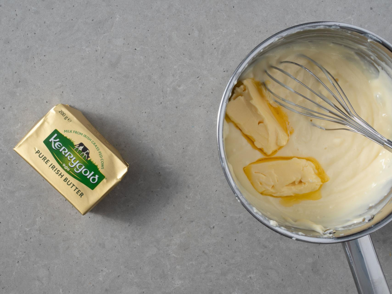 Ugotowany budyń w garnku. Obok kostka masła.