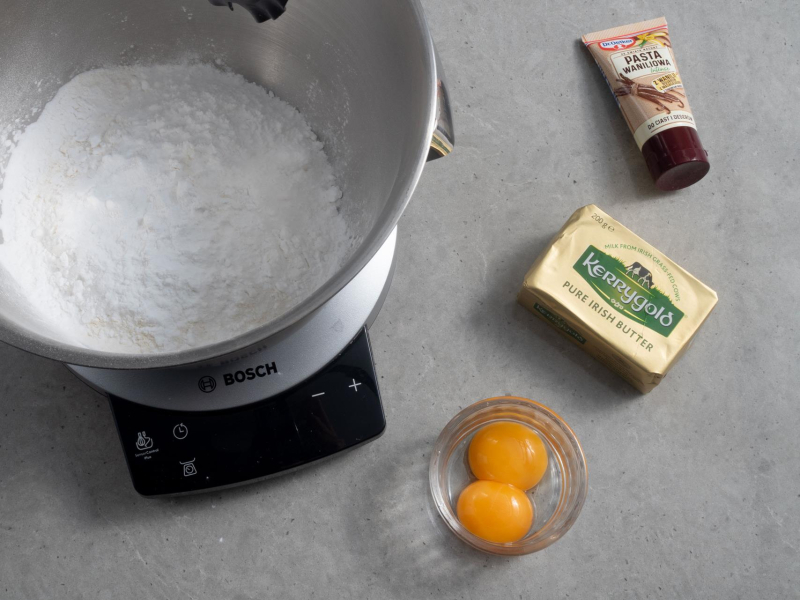 Na blacie kuchennym robot kuchenny firmy Bosch. Obok  masło Kerrygold, żółtka, , pasta waniliowa
