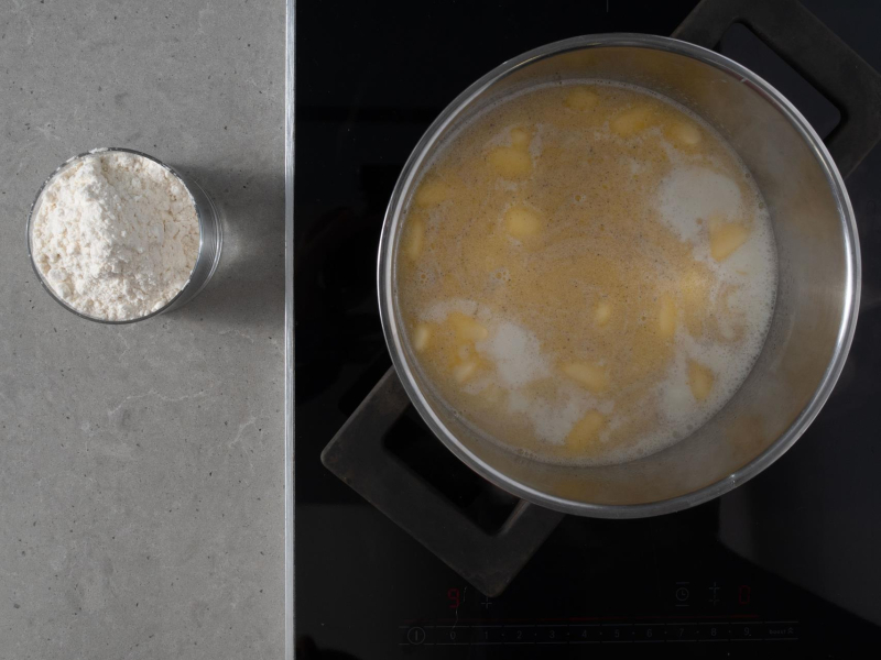 W garnku gotujące się mleko z wodą i masłem. Obok miseczka z mąką.