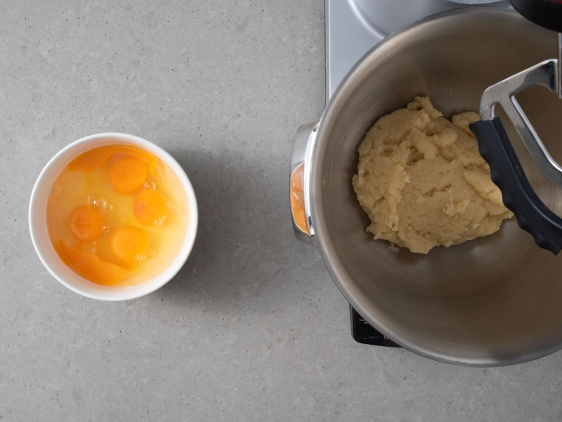 Ciasto parzone przełożone do misy miksera. Obok jajka w miseczce.