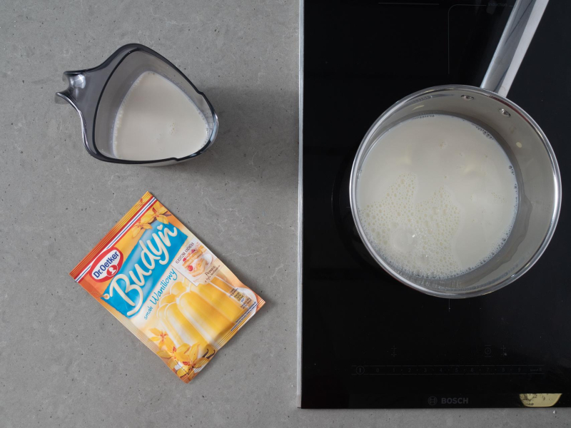 Na blacie opakowanie budyniu waniliowego. Obok w garnku mleko.