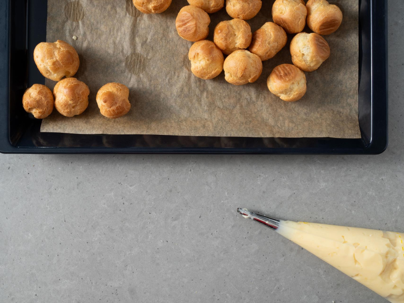 Upieczone ptysie i rękaw cukierniczy z kremem budyniowym.