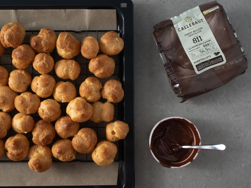 Rozpuszczona czekolada w miseczce. A obok upieczone profiterole.