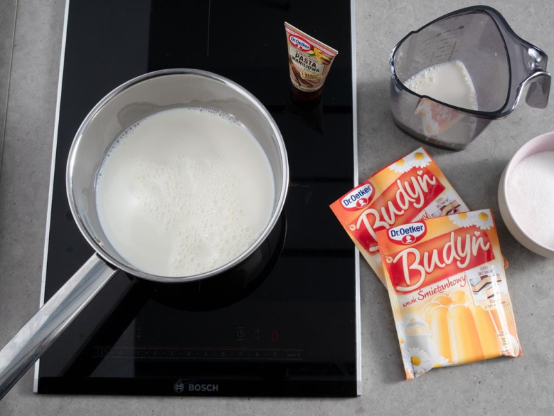 na płycie rondelek z mlekiem do gotowania kremu budyniowego obok budynie Dr. Oetker