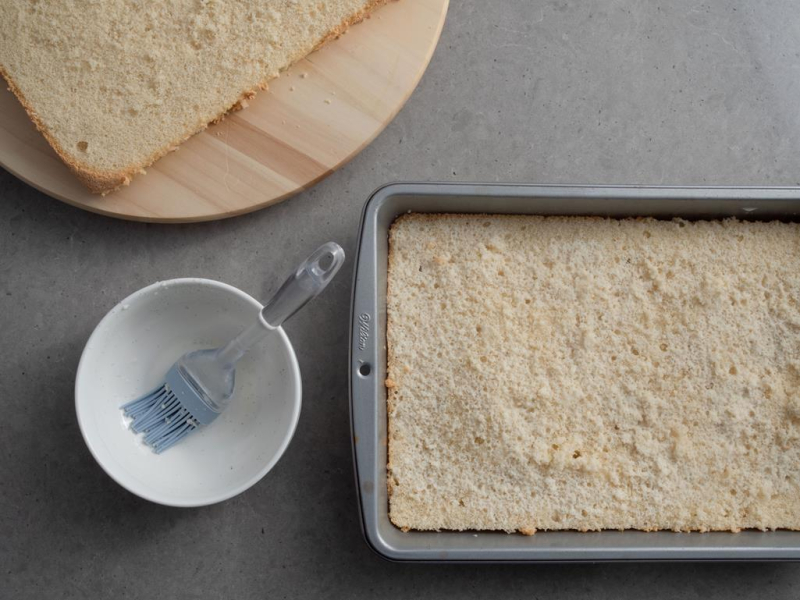 w formie przekrojony biszkopt na dwa blaty obok miseczka z ponczem i pędzelkiem do nasączania